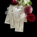 Small perfume bottles with gold caps on decorative cards, surrounded by flowers.